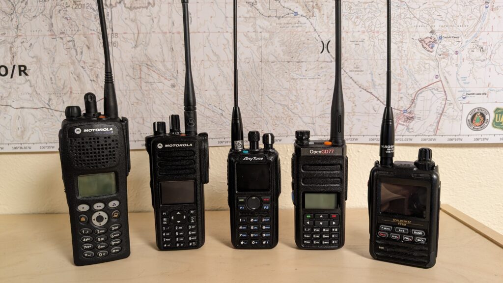 Photo of 5 handheld radios on a shelf: Motorola XTS2500, Motorola XPR7550e, Anytone 878 UV Plus II, Radioddity GD77, Yaesu FT-5DR