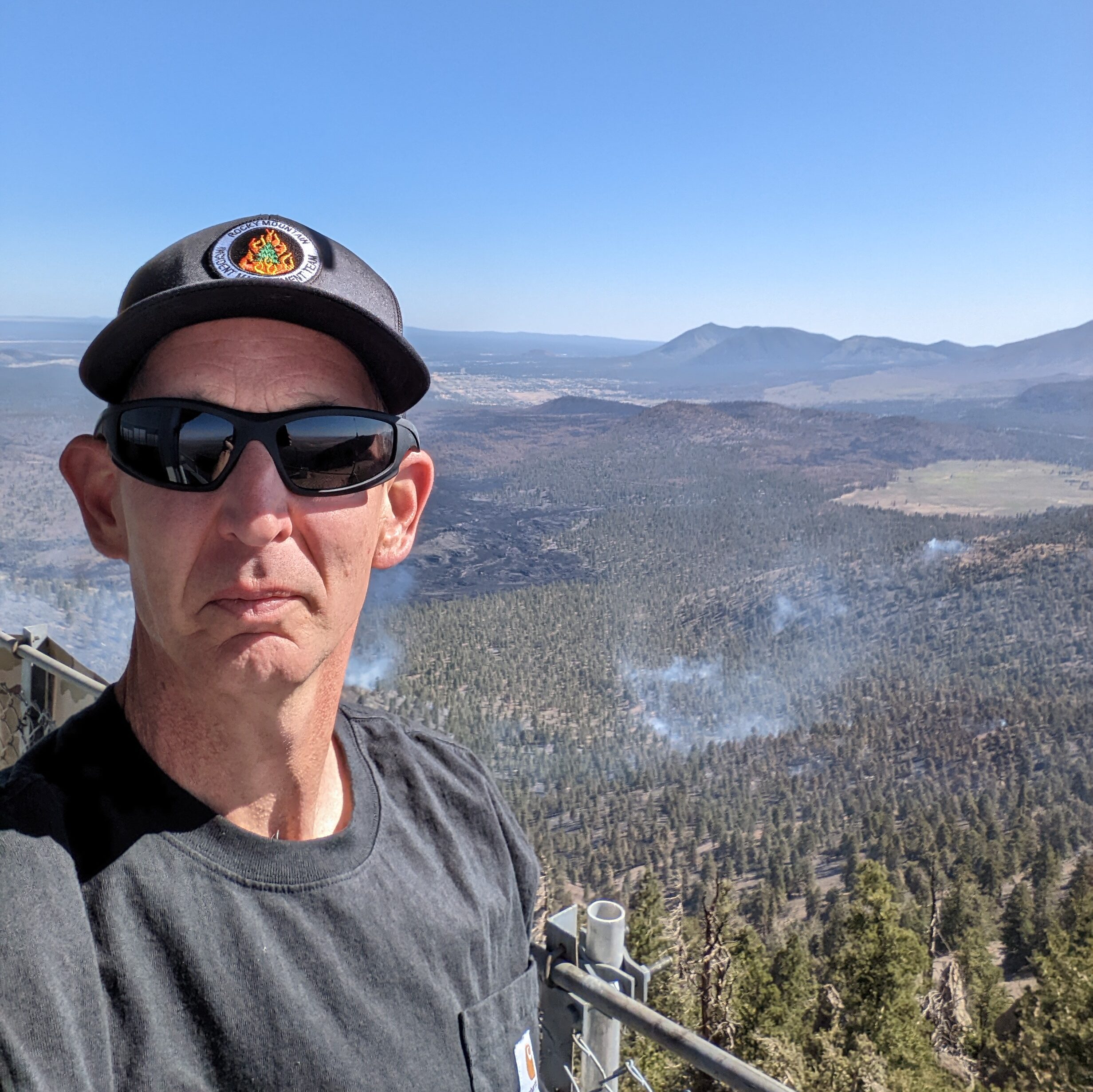 Bud standing on a fire tower in Arizona with the Pipeline fire smodlering in teh background.